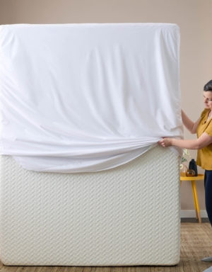 mattress protector fitted over mattress by woman in bedroom – breathable bed protection cover by Cover & Protect Australia